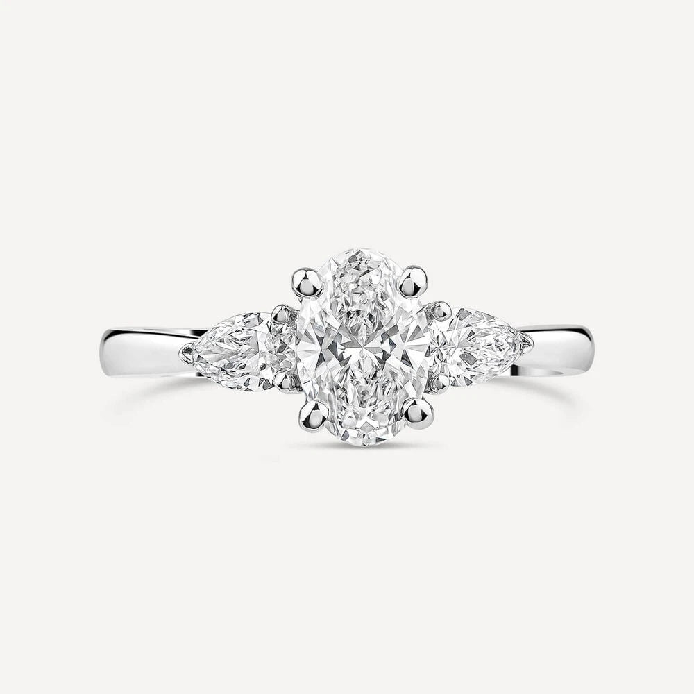 Platinum engagement ring featuring an oval-cut center diamond flanked by two pear-shaped side diamonds, set on a polished band.