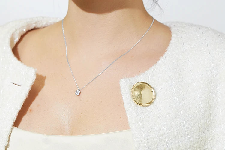Woman wearing a cream textured jacket with a large gold button and a delicate pendant necklace featuring a single round diamond on a fine chain.