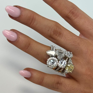hand with pink manicure showcasing multiple diamond rings in various styles