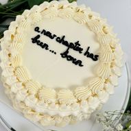 White cake with decorative frosting and text that says A New Chapter has been born.